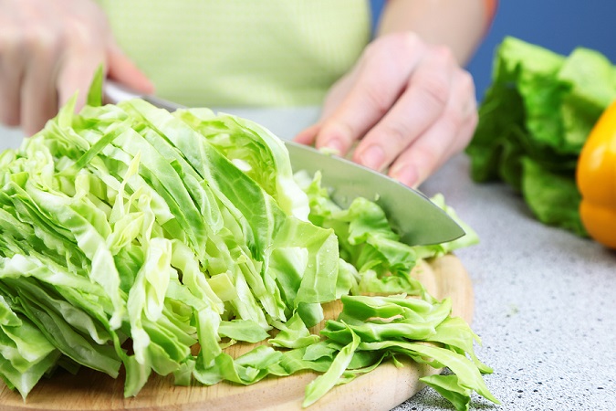 Female hands chopped cabbage on wooden board, close-up, on blue